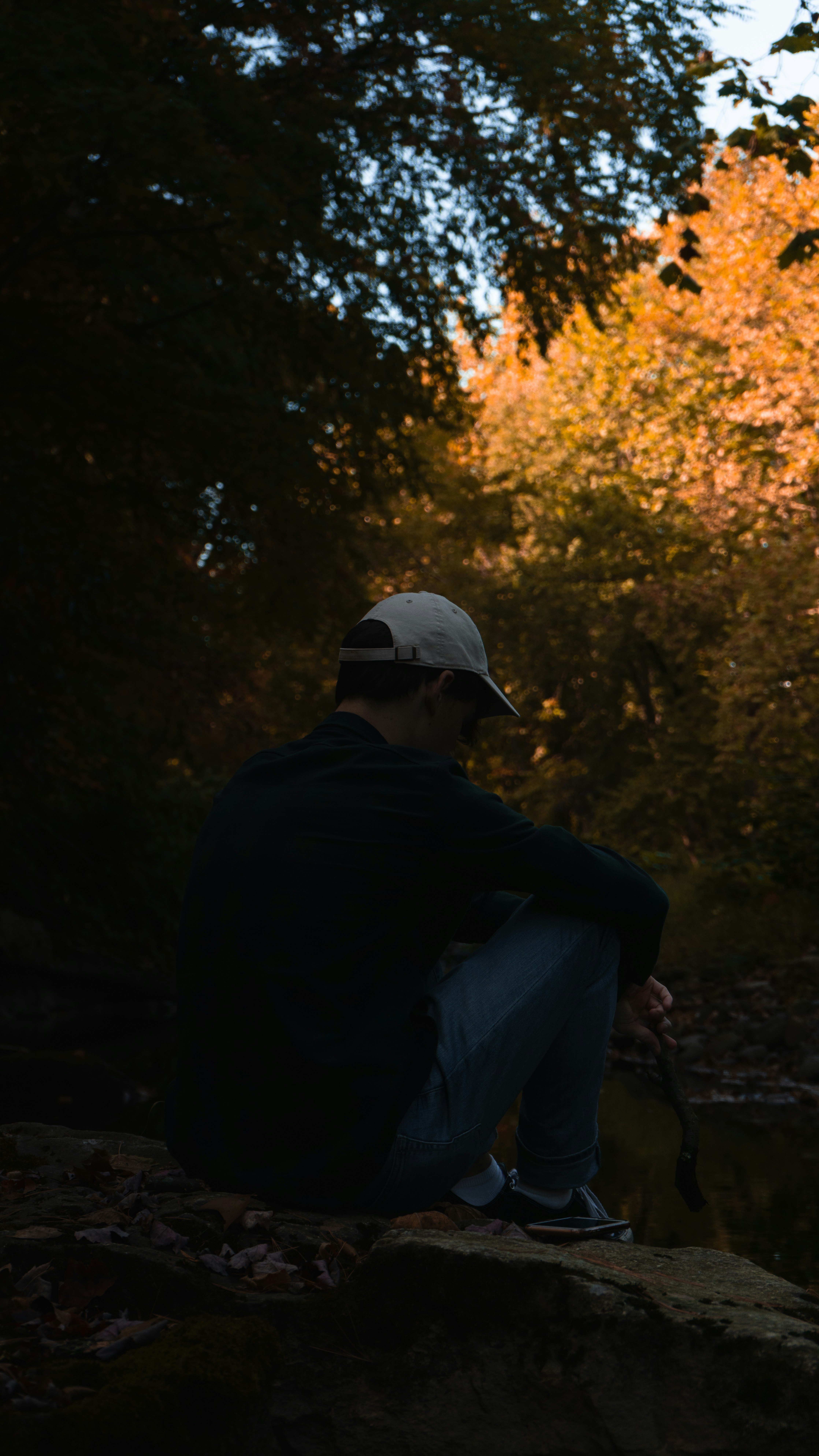 man in black jacket and white cap sitting on rock